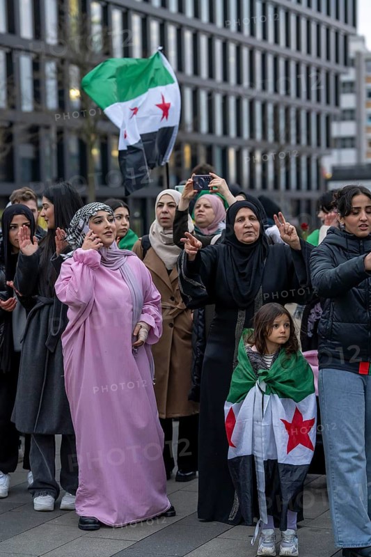 Syrian woman celebrate the end of the Assad regime after the change of power in Syria at a rally on the square in front of the main railway station in Duisburg, North Rhine-Westphalia, Germany