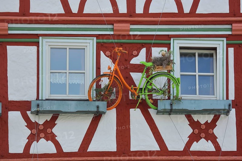 Brown-red house facade with floral decoration and colorful bicycle, two windows, half-timbered house, market square, Meiningen, Thuringia, Germany