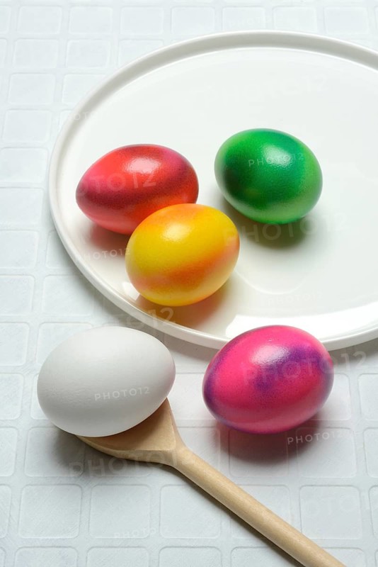 Coloured eggs on a plate and uncoloured eggs on a spoon, Easter celebration