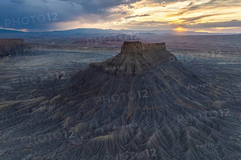 A breathtaking aerial view of a sunset gracing the unique and dramatic erosion of Factory Butte in Utah, highlighting the natural beauty and desolation of the area