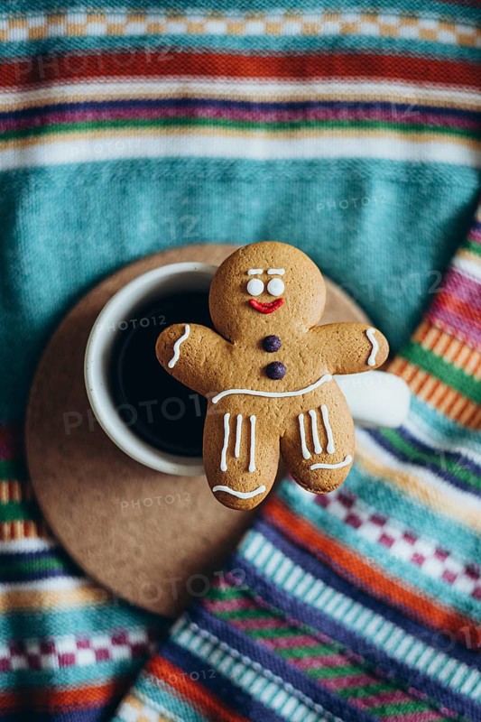 Charming gingerbread man cookie rests on a coffee cup, set against a vibrant, striped fabric background Perfect cozy, festive, and warm holiday scene
