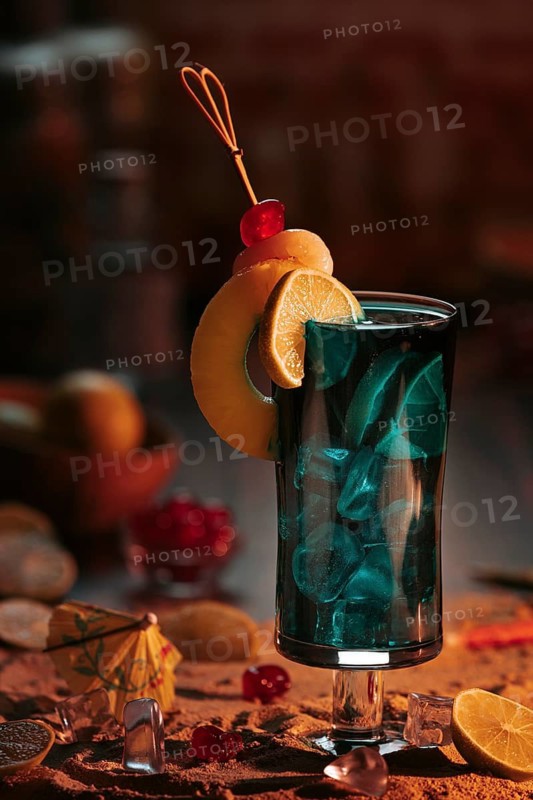 Cocktail in a glass with ice cube cubes, decorated with lime slices and cherries on a sandy background in a sunset atmosphere