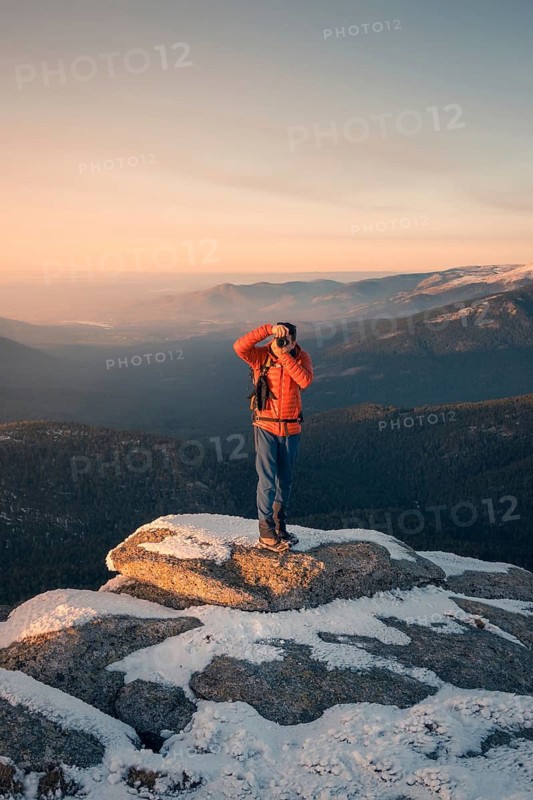 A person in vibrant attire photographs the snow-dusted peaks of Siete Picos, set against the serene backdrops of Madrid's Guadarrama Mountains at sunrise