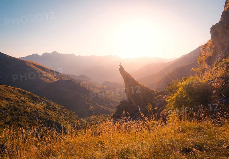 A lone figure stands triumphantly on a rock pinnacle amidst a stunning mountain landscape bathed in the golden hues of sunrise, capturing the essence of adventure and freedom in the Pyrenees