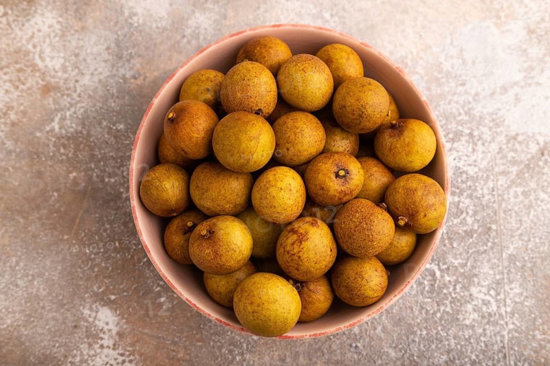 Ripe Longan in ceramic bowl on brown concrete background, top view, flat lay, close up, minimalism
