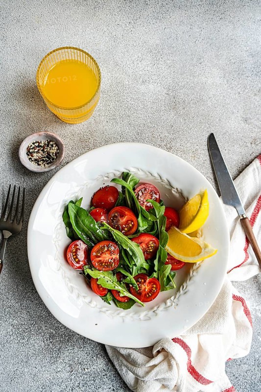 A fresh arugula and herb salad featuring cherry tomatoes, seeds, and Himalayan salt, drizzled with olive oil. Perfectly vibrant and healthy for any meal