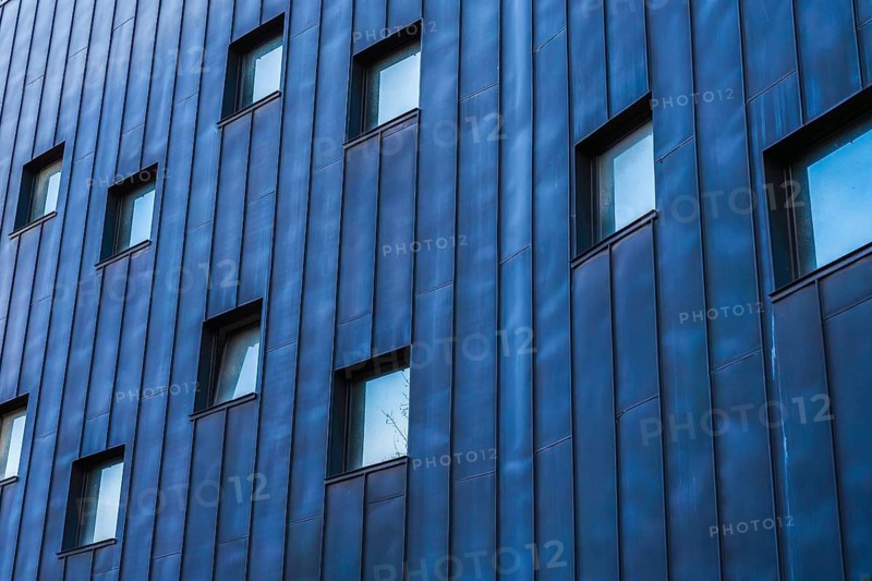 A contemporary building showcasing a multicolored facade, emphasized by a pattern of blue-tinted metallic panels, punctuated by rectangular windows