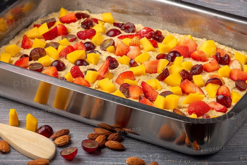 Unbaked fruit cake in the shape of topped with mango, strawberries and grapes