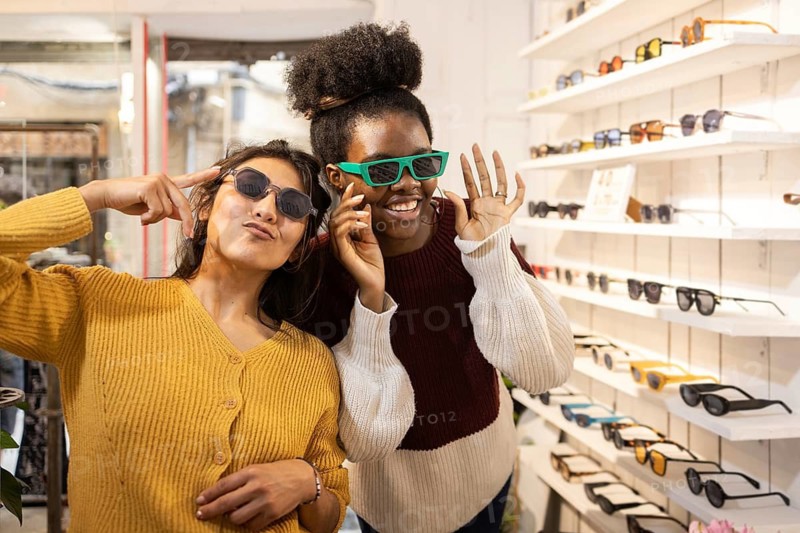 Two friends showcase trendy sunglasses in a stylish store. The vibrant setting features an array of frames, highlighting the latest eyewear fashion for a confident look