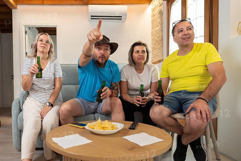 Group of friends celebrating a goal while watching a soccer match on TV at home. Happy emotions, cheering, beer, snacks and friendship during sports entertainment