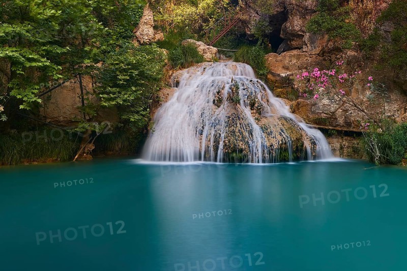 A small waterfall flows into a calm turquoise blue pool, surrounded by flowers and rocks, waterfalls, ponds, Polylimnio, Peloponnese, Greece