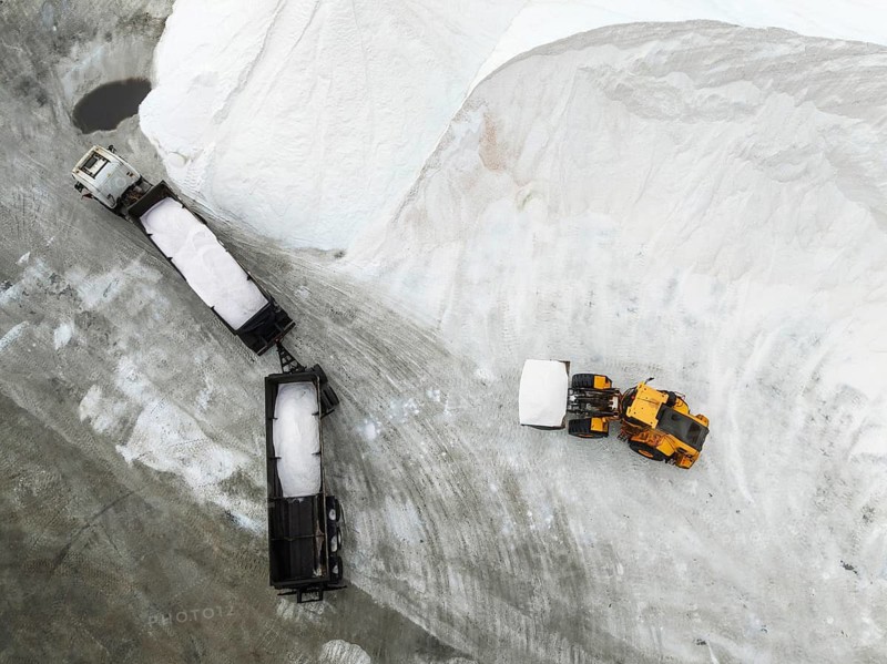 Lorry and excavator at the salt heaps of the Walvis Bay Salt works. Aerial view. Drone shot. Walvis Bay, Namibia