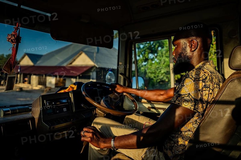 PAJE, ZANZIBAR - OCTOBER 18, 2025: A local African man driving a bus through a Zanzibar village, captured in warm golden hour light through the truck cabin window