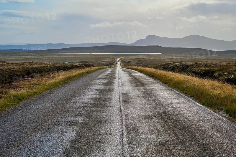 Deserted road leads through vast landscape with mountains in the background and overcast sky, Tongue, Lairg, Scotland, United Kingdom, Great Britain