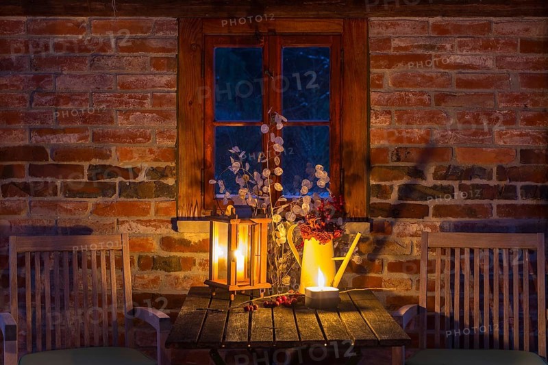 Still life with candles on a table, chairs next to it, it's getting dark outside, cozy atmosphere at dusk, winter evening