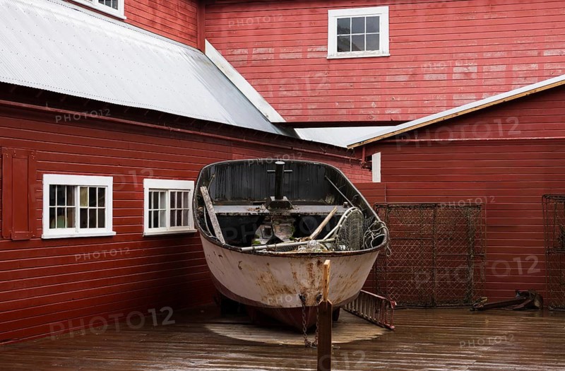 An old, weathered boat stands on display against a vibrant red wooden building in Hoonah, Alaska, reflecting the maritime heritage of the Tlingit community on Chichagof Island