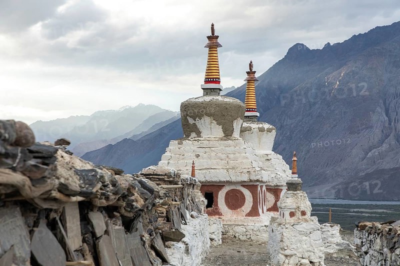 Ancient stupas stand against the backdrop of majestic mountains and a dramatic sky in Diskit, Nubra Valley, India, showcasing rich cultural heritage and breathtaking scenery