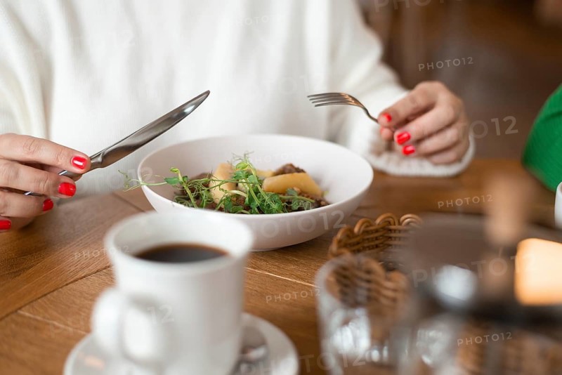 Close-up of a woman savoring a breakfast dish with a cozy ambiance in a cafe. The table setting includes a bowl of mushroom cutlets with potatoes and fresh greens