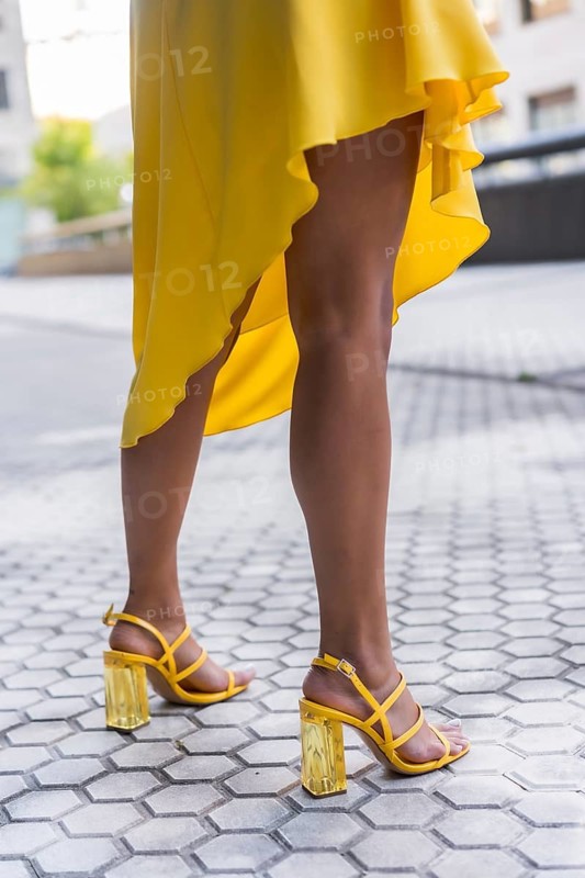 Vertical cropped photo of the sensual legs of a woman wearing yellow dress heels