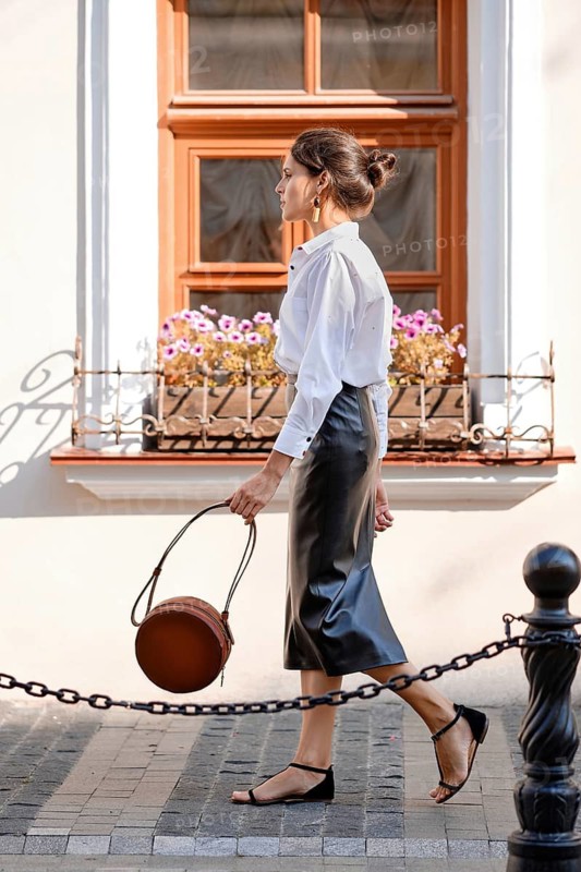 Elegant lady in leather skirt and white shirt walking down the street with leather hand bag
