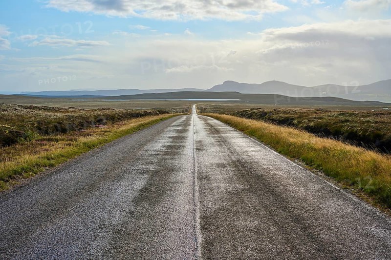 A long, empty road leads through a vast landscape of distant mountains under a cloudy sky, Tongue, Lairg, Scotland, United Kingdom, Great Britain