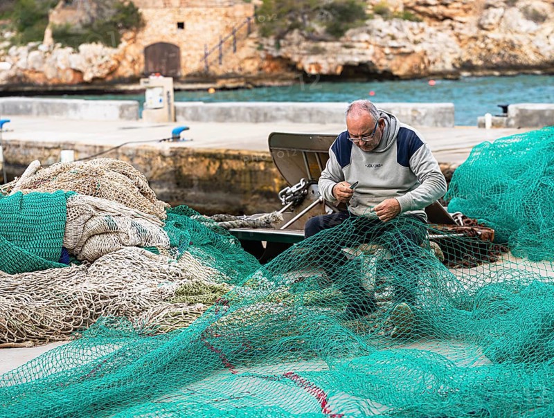 A fisherman ties and repairs his net in the port of Cala Figuera, Majorca, Spain