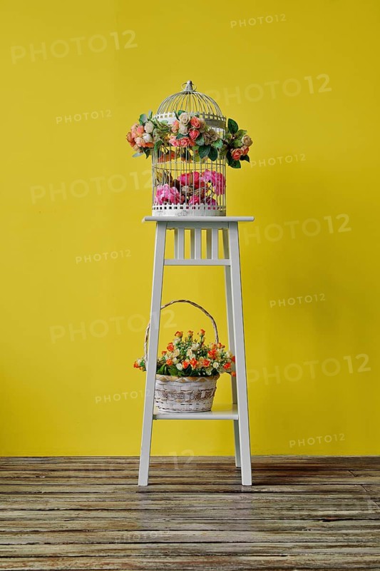 Decoration of the room with birdcage and basket with frlowers on white wood chair near yellow wall background. Empty place for text