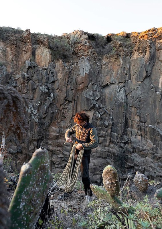 A climber prepares for a traditional climbing adventure on a rugged cliff side, surrounded by nature. The scene captures the essence of outdoor exploration and adventure