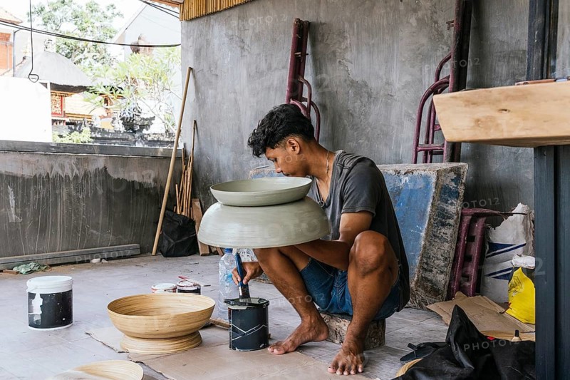 Balinese artist painting sculptures in a traditional setting, showcasing cultural craftsmanship. The ambient workshop setting highlights the dedication to art