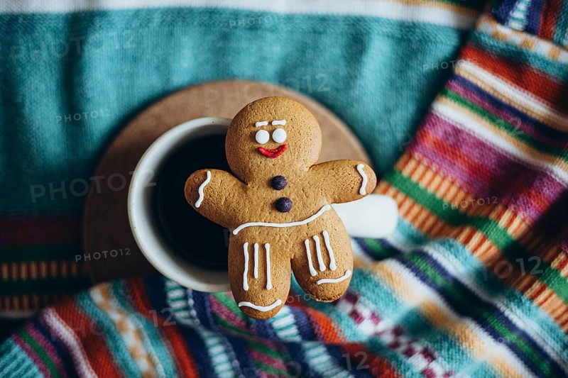 Charming gingerbread man cookie adorns a cup of coffee The vibrant patterned fabric beneath enhances a cozy, festive atmosphere, perfect for holiday-themed visuals