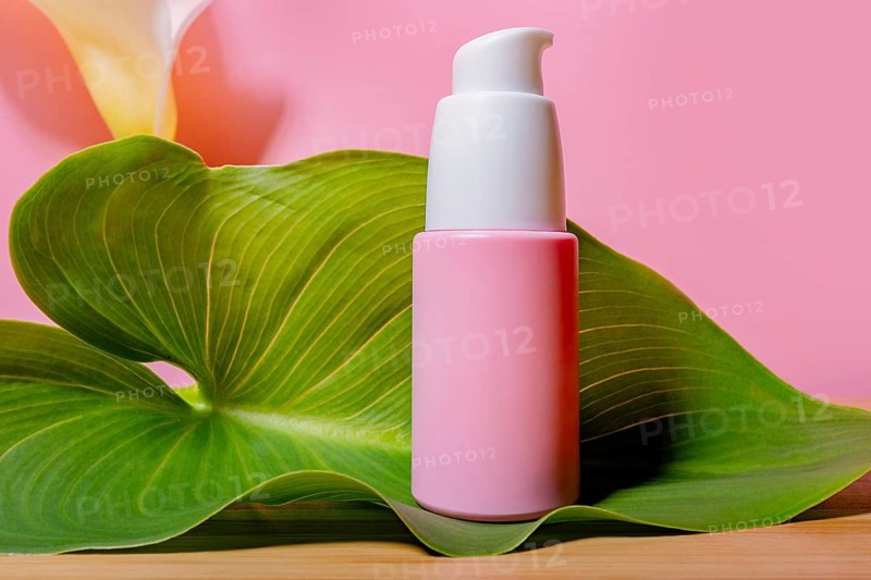 A pink skincare product bottle with a pump dispenser rests elegantly on a green, lush leaf, against a soft pink background, evoking a sense of nature and beauty