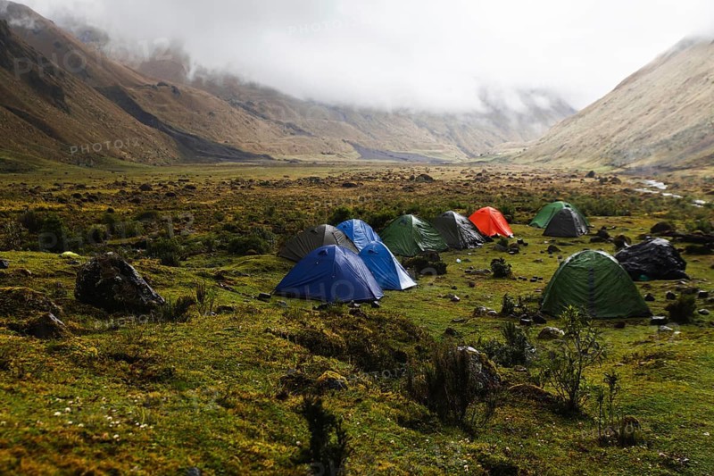 A group of colorful tents set up in a remote Andean valley at El Altar volcano, Ecuador, surrounded by misty mountains, lush greenery, and a peaceful wilderness atmosphere