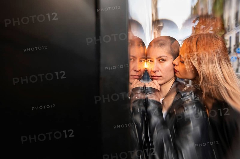 An intimate portrait of a lesbian couple sharing a tender moment, reflecting in glass. The artistic effect adds depth, capturing the beauty of their bond in a unique way