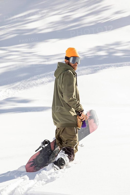 A snowboarder in an orange helmet and green jacket navigates through pristine powder in a remote mountain setting. Perfect representation of extreme winter sports in its natural environment