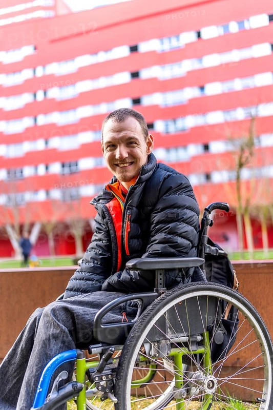 Happy man with disability sitting in wheelchair, enjoying sunny day outdoors, promoting inclusivity and positive representation of people with disabilities