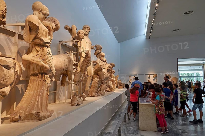 West pediment of the Temple of Zeus, battle between lapiths and centaurs, museum exhibition with ancient sculptures and group of visitors looking at the exhibits, Olympia Archaeological Museum, Ancient Olympia, Olympia, Peloponnese, Greece