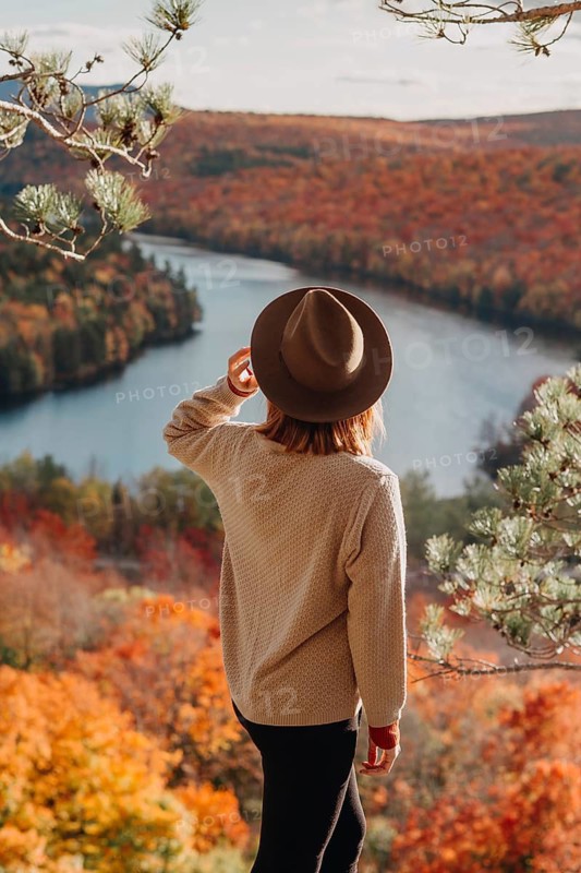 A woman gazes over a vibrant autumn landscape in Quebec, Canada. With colorful foliage and a winding river, the scene captures the essence of fall's natural beauty and tranquility