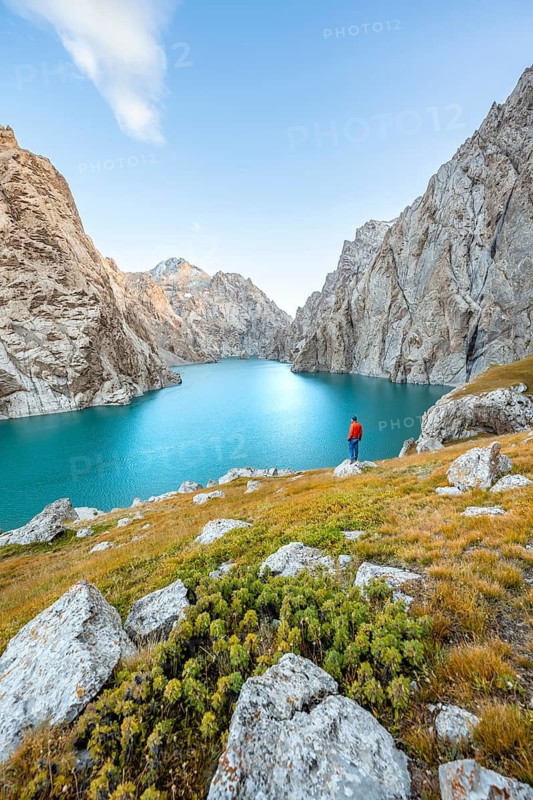 Young man at the turquoise mountain lake Kol Suu with rocky steep mountains, Kol Suu Lake, Sary Beles Mountains, Naryn Province, Kyrgyzstan
