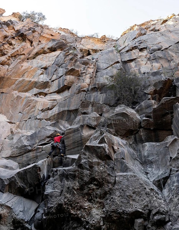 Two climbers takes on the challenge of a steep, rocky cliff in a rugged natural landscape. The image captures the essence of adventure and the beauty of untouched nature