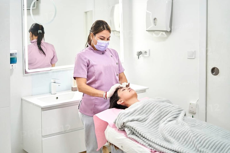 A skilled practitioner provides a relaxing facial treatment to a client in a well-lit aesthetic medicine clinic. The calming environment enhances the overall beauty experience for the client