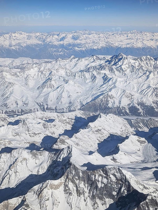 Stunning aerial view of a vast, snow-covered mountain range captured from an airplane, showcasing the majestic peaks and rugged ridges under a clear blue sky