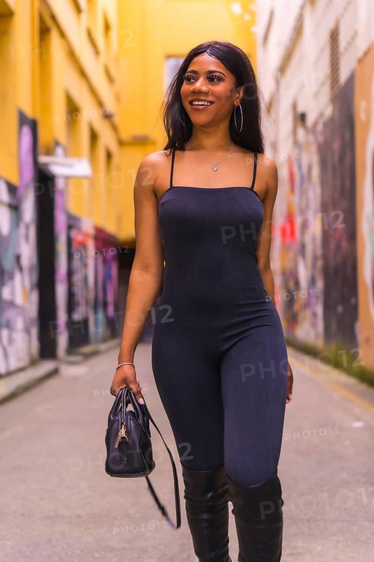 Urban style of a fashionable black girl in a black suit and high boots on a city street. Walking with a bag