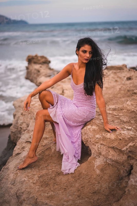 Posing of a young brunette Caucasian in a pink dress, on the beach having fun by the sea