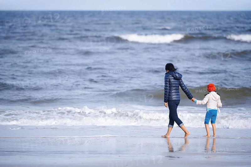 A mother and daughter holding hands, walking on a peaceful beach of California, United States. The gentle waves and soft sand create a tranquil scene of bonding and lifestyle
