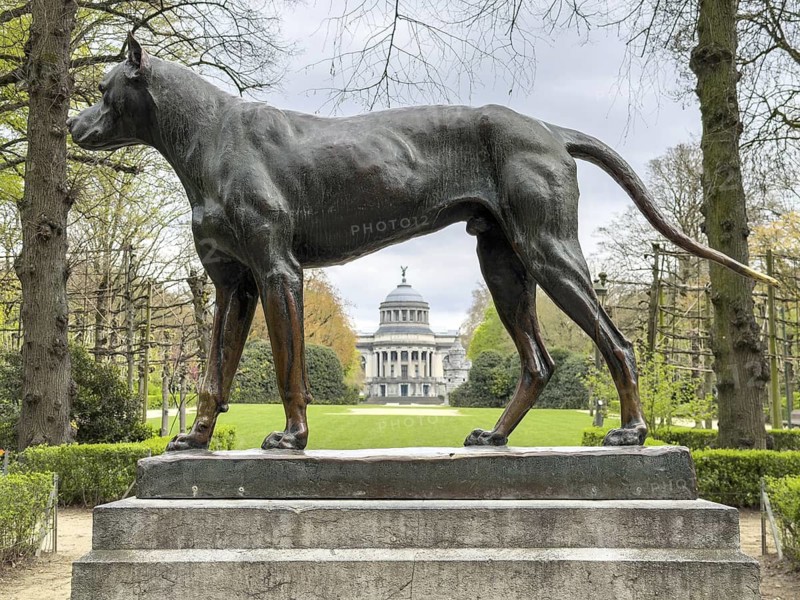 Bronze statue of a dog (Le Chien) by Jean-Baptiste Van Heffen in the Jubelpark (Parc du Cinquantenaire) with the Pavilion of Human Passions in the background, Brussels, Belgium