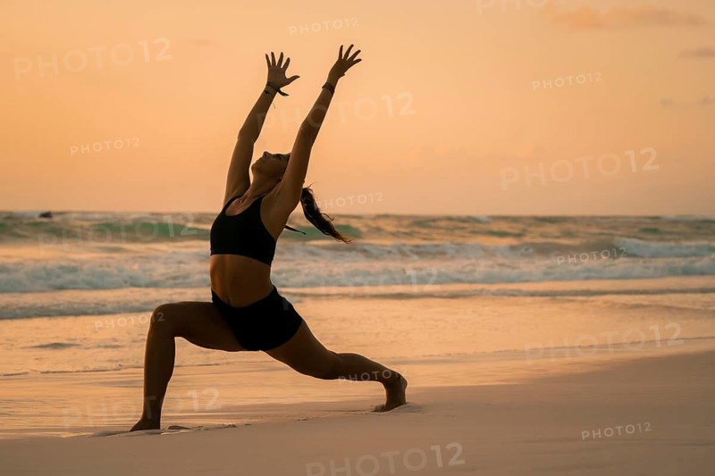 A woman gracefully practices yoga on a serene beach at sunset in Tulum, Mexico. The calming waves and warm colors create a peaceful atmosphere, embodying balance and tranquility