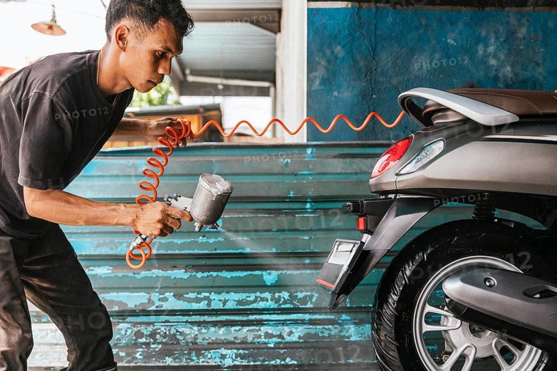 A motorcycle cleaner uses a spray gun to carefully wash a scooter inside a workshop. The attention to detail highlights the importance of cleanliness and maintenance for bikes