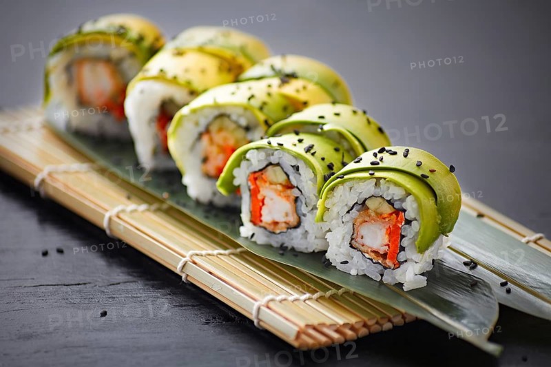 A delectable array of avocado-wrapped sushi rolls, topped with black sesame seeds, presented on a bamboo mat on a dark slate background
