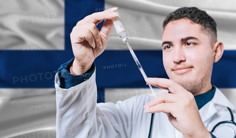 Doctor holding syringe on Finland flag background. Medical professional holding syringe with Finnish flag in the background