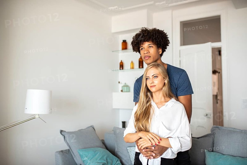 A couple shares a tender embrace in their stylish living room. Soft lighting and modern decor create a warm and inviting atmosphere, highlighting their bond